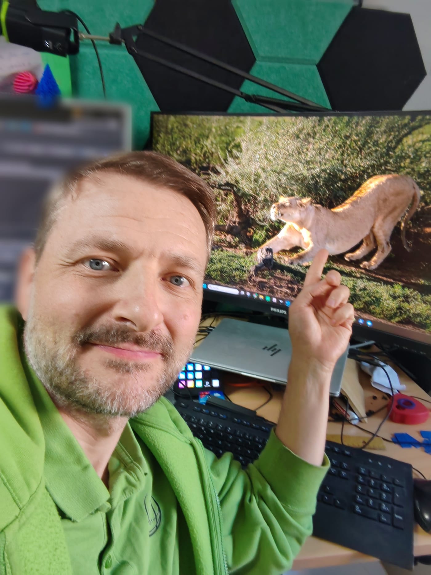 Martin Reichl am Schreibtisch im Büro zeigt lachend auf seinen Monitor