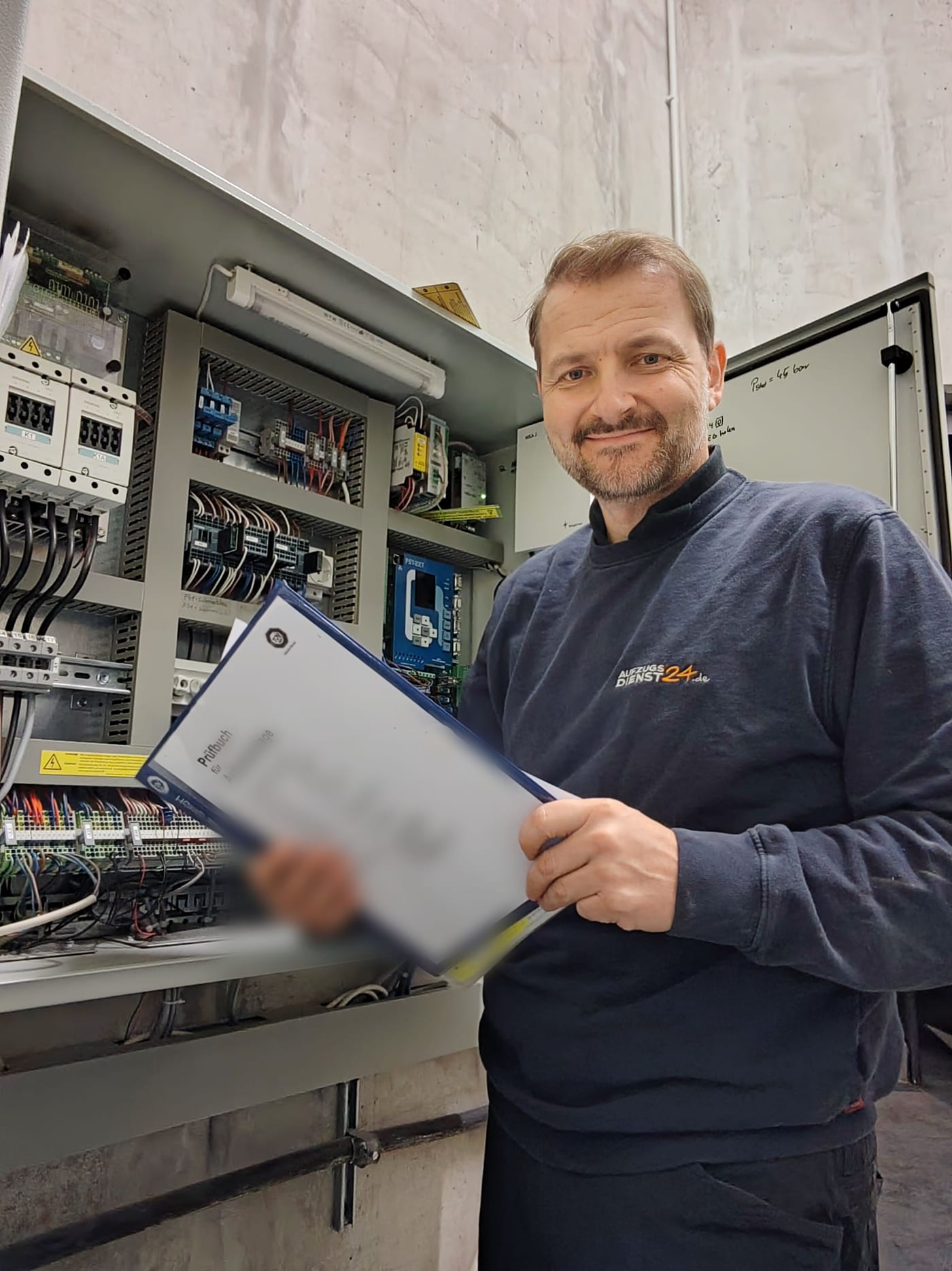 Martin Reichl mit dem Prüfbuch einer Aufzugsanlage vor einem geöffneten Schaltschrank