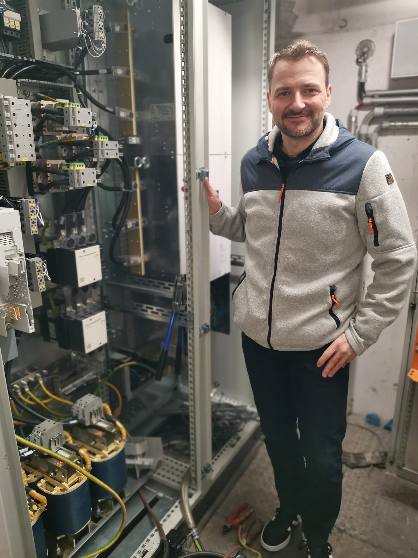 Martin Reichl steht in einem Technikraum neben einem geöffneten Schaltschrank